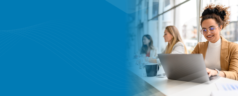 Smiling businessperson uses charity finance software on a laptop at an office table, with colleagues in the background